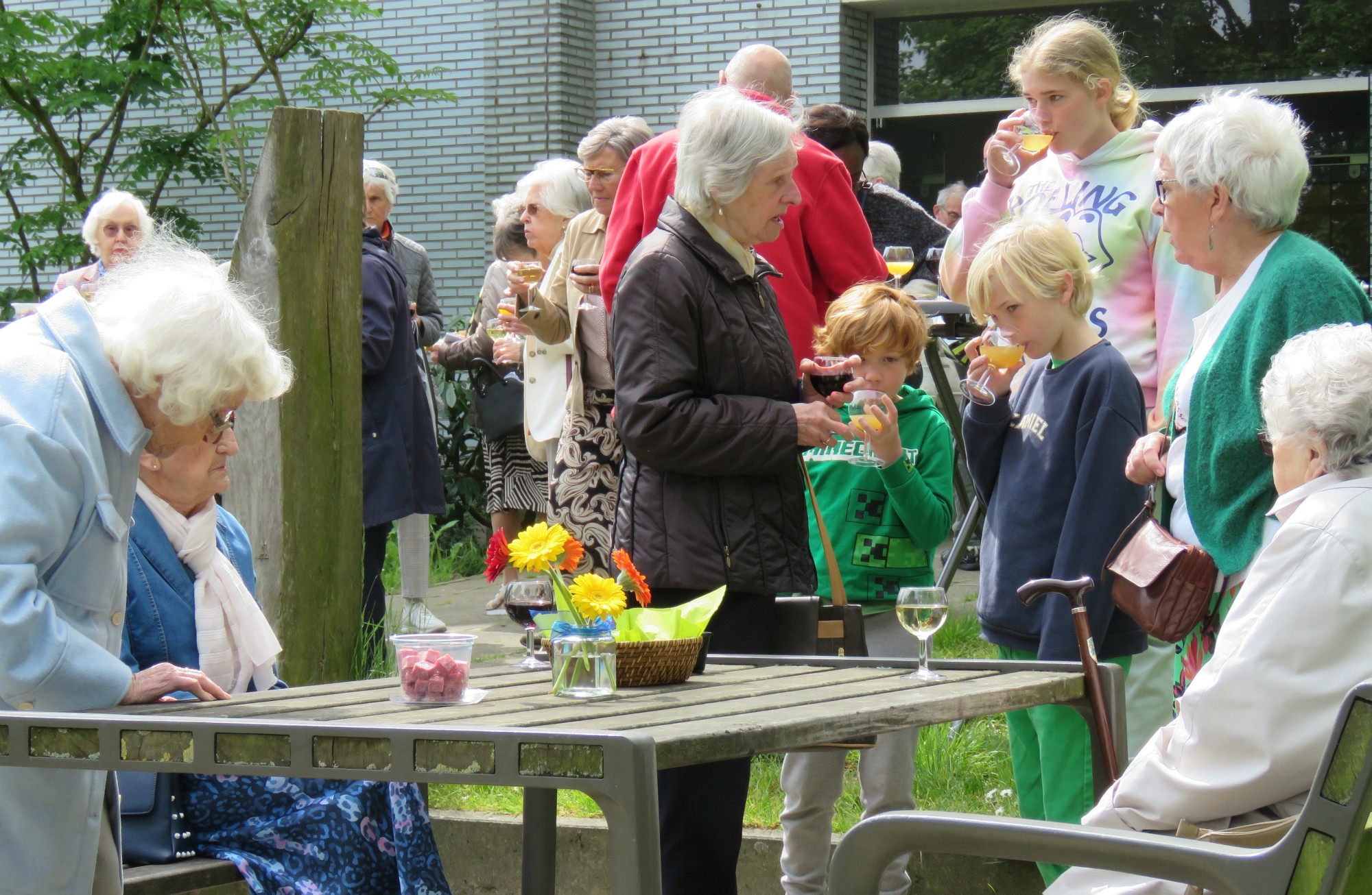 Receptie met deelmoment na de vieiring buiten in de zon aan de Sint-Anna-ten-Drieënkerk, Antwerpen Linkeroever