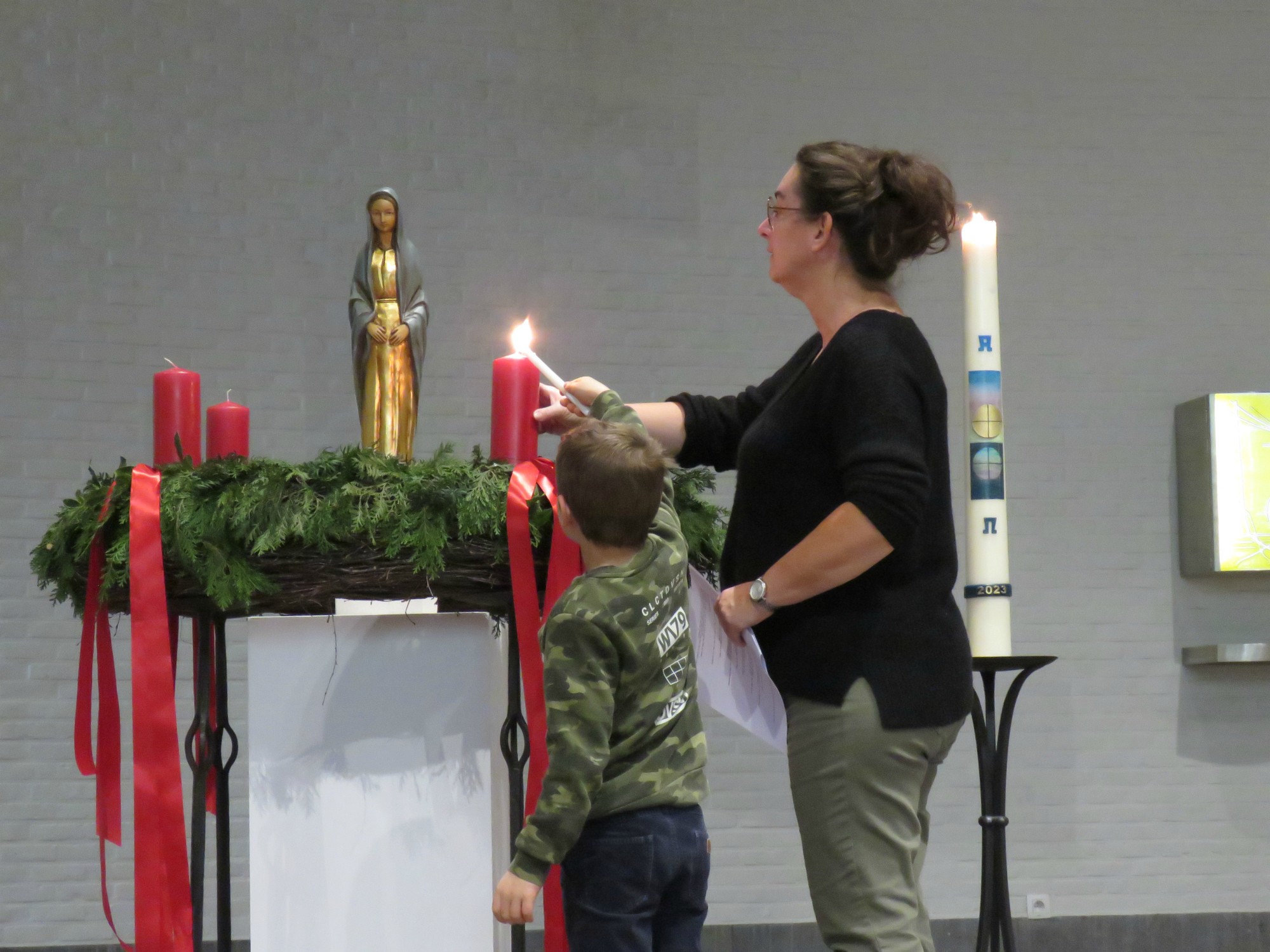 De eerste kaars van de adventskrans wordt aangestoken door een eerste communicant